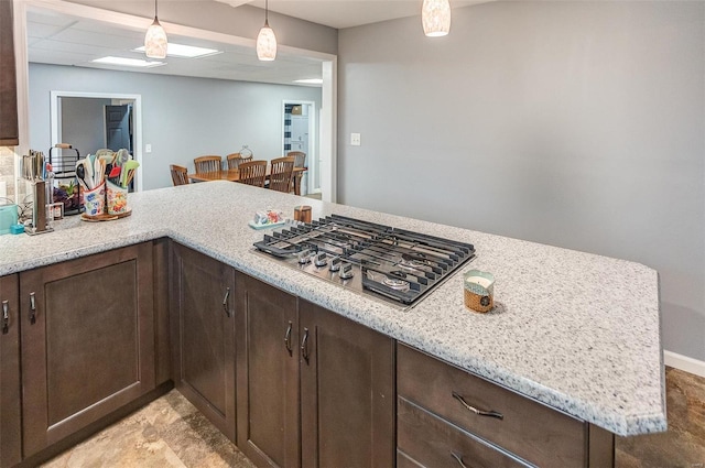 kitchen featuring dark brown cabinetry, light stone countertops, stainless steel gas cooktop, decorative light fixtures, and kitchen peninsula