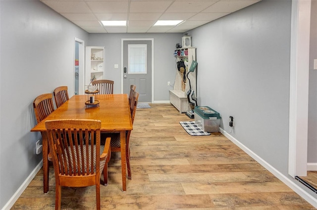 dining area with a paneled ceiling and light wood-type flooring