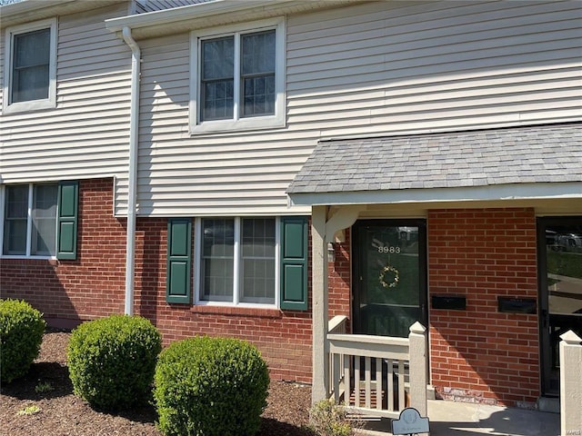 doorway to property featuring brick siding and a shingled roof