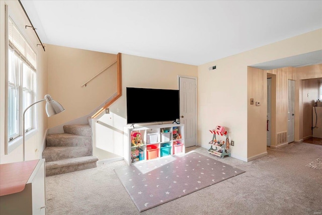 unfurnished living room featuring a wealth of natural light, visible vents, stairs, and carpet floors