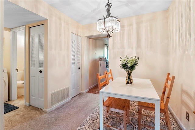 carpeted dining space featuring visible vents, baseboards, and a chandelier