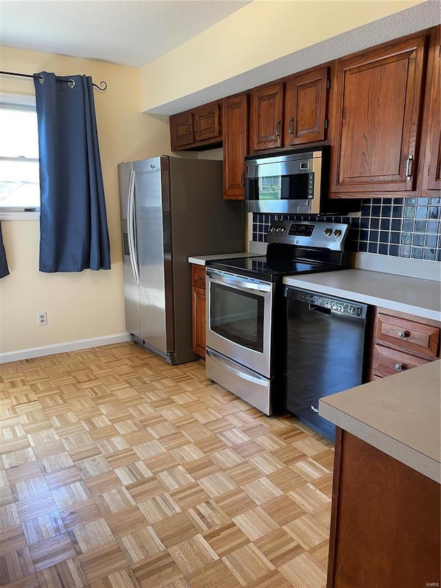 kitchen with backsplash, baseboards, light countertops, brown cabinets, and stainless steel appliances