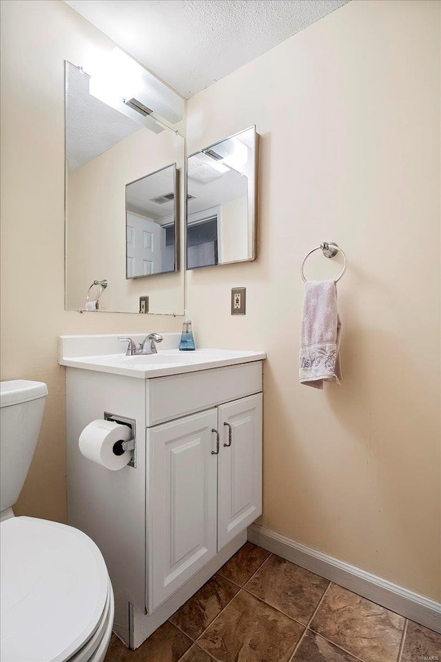 half bathroom with toilet, a textured ceiling, tile patterned flooring, baseboards, and vanity