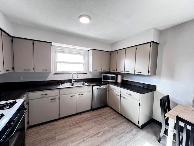 kitchen with dark countertops, appliances with stainless steel finishes, gray cabinetry, light wood-style floors, and a sink