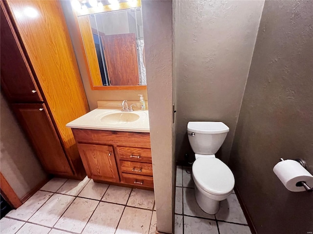 bathroom with a textured wall, vanity, toilet, and tile patterned floors