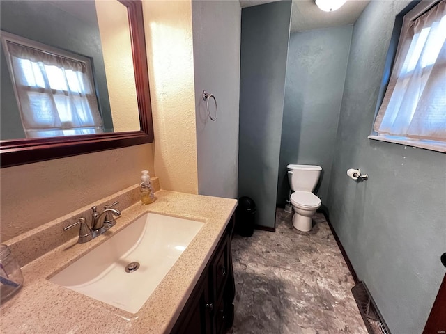 bathroom with a textured wall, vanity, and toilet