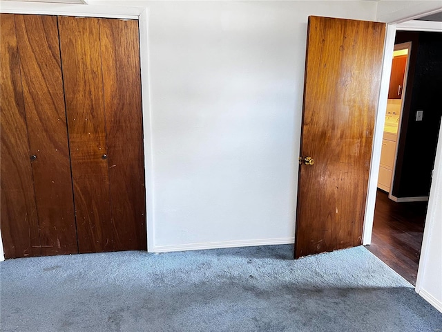 unfurnished bedroom with baseboards, dark carpet, and a closet