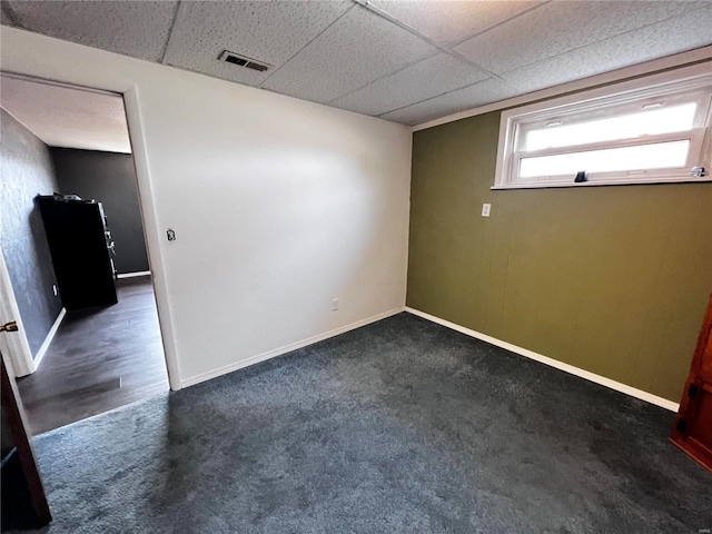 empty room with dark colored carpet, visible vents, a paneled ceiling, and baseboards