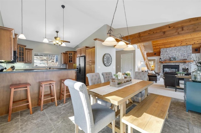 dining room with vaulted ceiling, a stone fireplace, and a ceiling fan