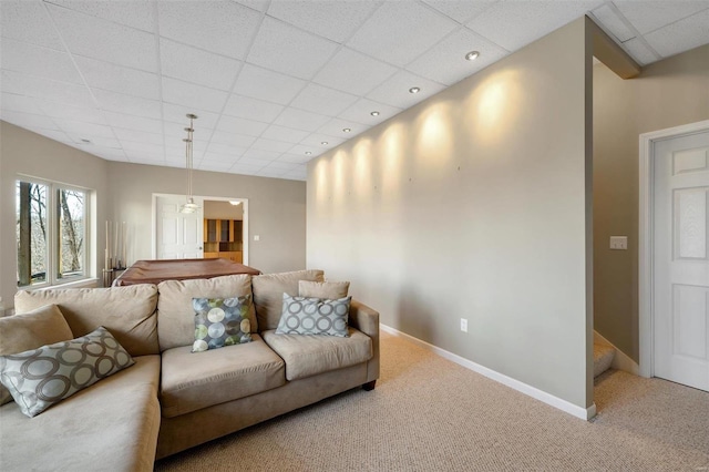 carpeted living area featuring a paneled ceiling and baseboards