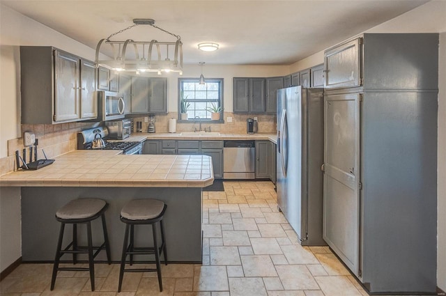 kitchen with decorative light fixtures, a kitchen bar, decorative backsplash, kitchen peninsula, and stainless steel appliances