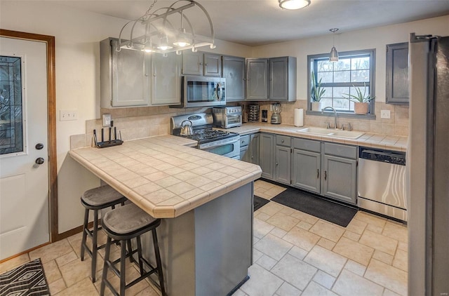 kitchen featuring hanging light fixtures, appliances with stainless steel finishes, gray cabinetry, and kitchen peninsula