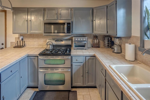 kitchen with sink, gray cabinetry, tile countertops, stainless steel appliances, and decorative backsplash