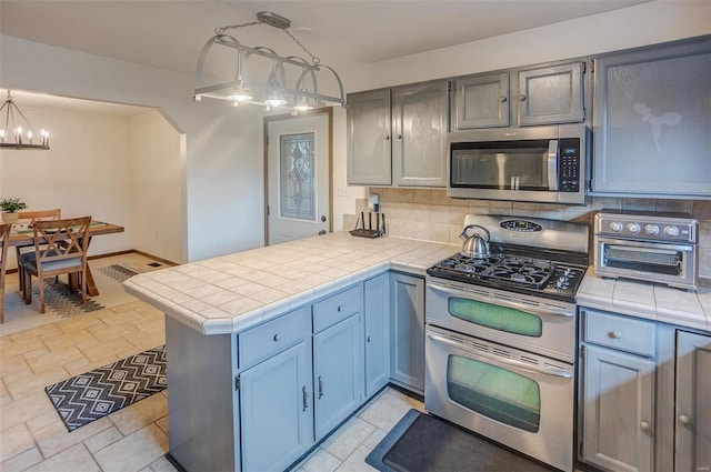 kitchen featuring appliances with stainless steel finishes, tile counters, kitchen peninsula, pendant lighting, and backsplash