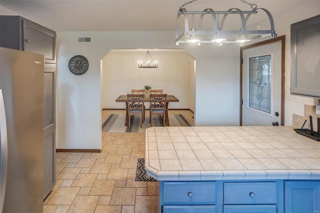 kitchen featuring hanging light fixtures, an inviting chandelier, tile countertops, and stainless steel refrigerator