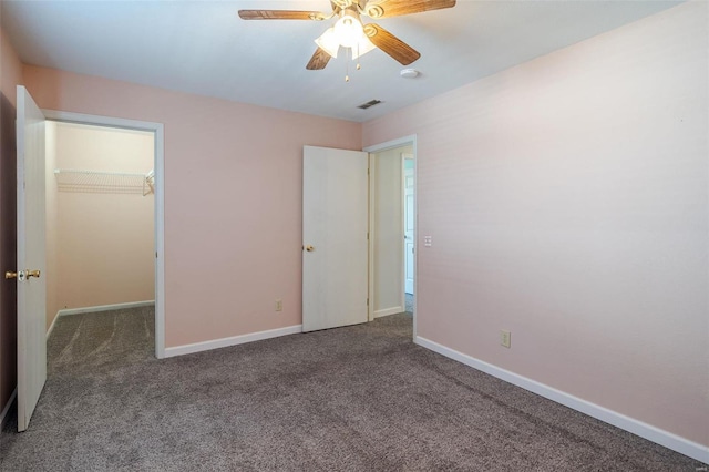 unfurnished bedroom featuring dark colored carpet, a walk in closet, ceiling fan, and a closet