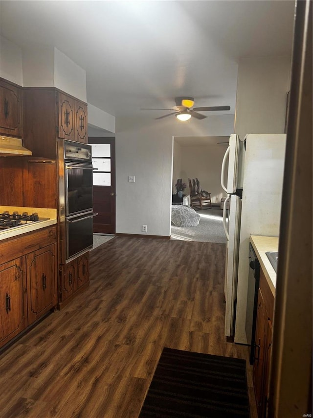 kitchen featuring gas stovetop, black double oven, dark wood-type flooring, and ceiling fan