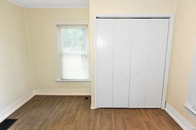 unfurnished bedroom featuring crown molding, dark wood-type flooring, and a closet