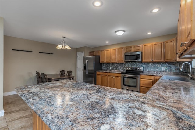 kitchen with appliances with stainless steel finishes, pendant lighting, sink, decorative backsplash, and kitchen peninsula