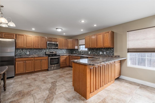 kitchen featuring appliances with stainless steel finishes, dark stone countertops, backsplash, hanging light fixtures, and kitchen peninsula