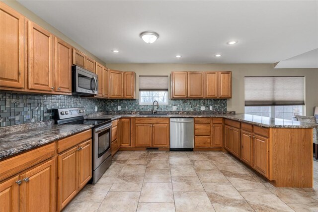 kitchen with sink, appliances with stainless steel finishes, dark stone countertops, tasteful backsplash, and kitchen peninsula