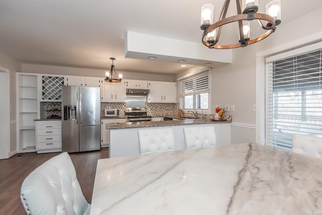 kitchen featuring dark stone countertops, decorative light fixtures, stainless steel appliances, and white cabinets