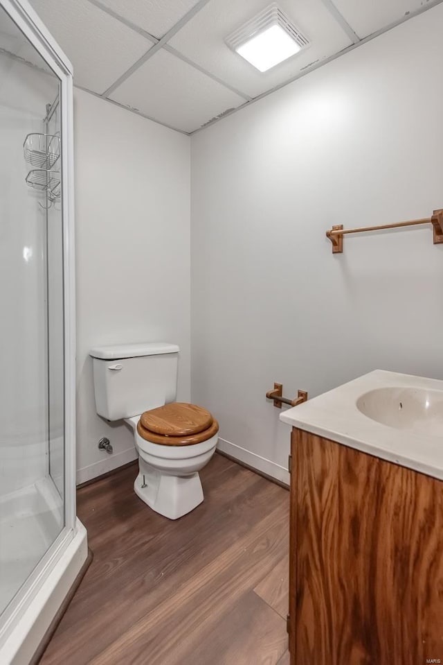 bathroom featuring a paneled ceiling, a shower with door, hardwood / wood-style floors, vanity, and toilet