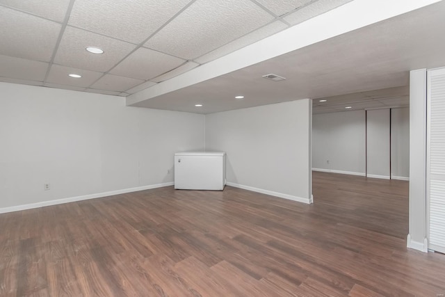 basement with a drop ceiling, dark hardwood / wood-style floors, and refrigerator