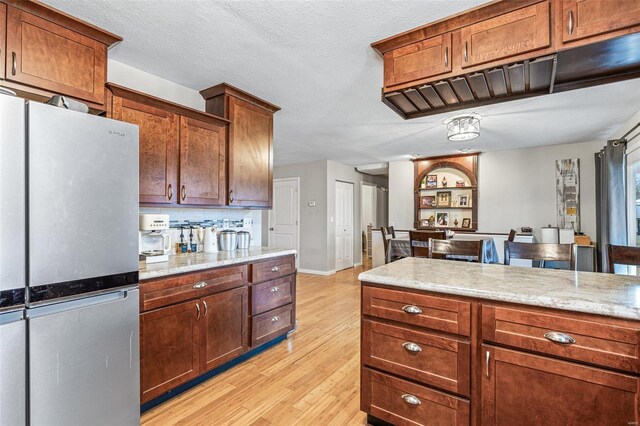 kitchen featuring backsplash, stainless steel fridge, light stone counters, light hardwood / wood-style floors, and a textured ceiling