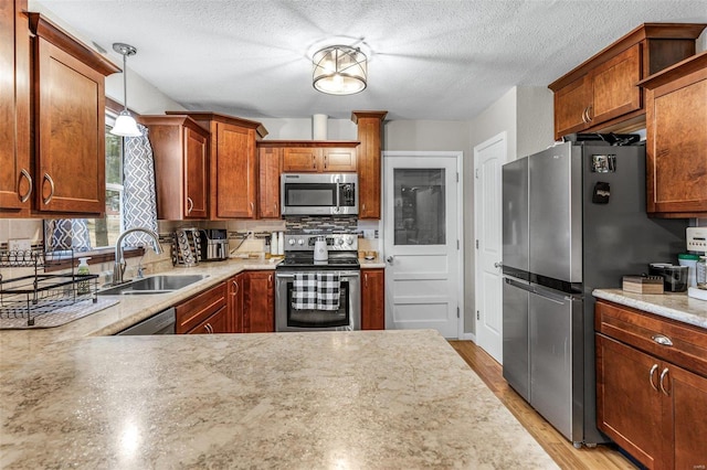 kitchen featuring pendant lighting, tasteful backsplash, sink, stainless steel appliances, and light hardwood / wood-style flooring