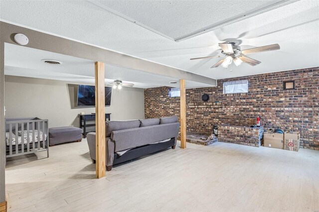 living room featuring ceiling fan, brick wall, a textured ceiling, and light hardwood / wood-style floors