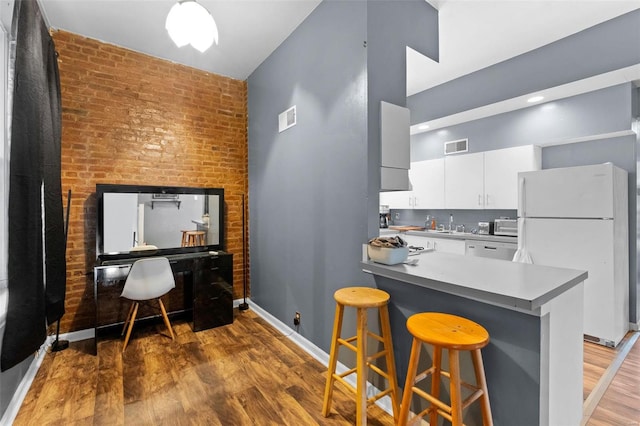 kitchen with a breakfast bar, white refrigerator, kitchen peninsula, hardwood / wood-style flooring, and white cabinets