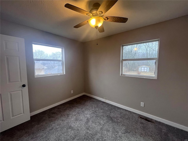 spare room featuring ceiling fan and dark colored carpet