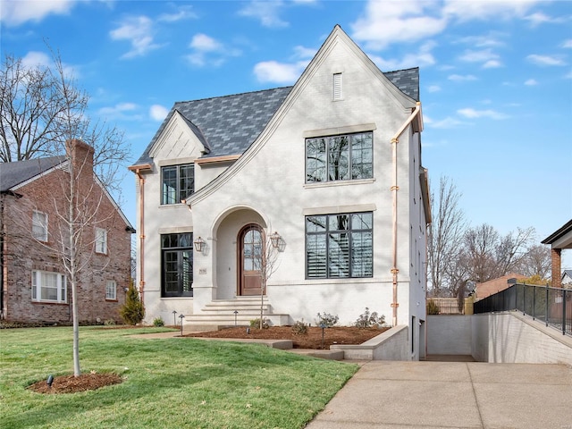 view of front of property featuring brick siding, fence, a front lawn, and stucco siding