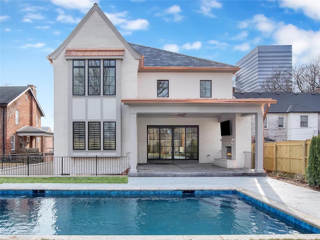 back of property featuring a warm lit fireplace, a patio, brick siding, and fence