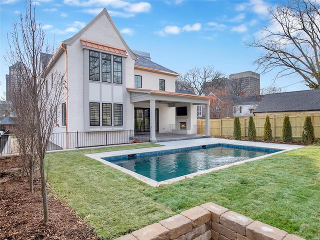 back of house with a warm lit fireplace, a lawn, fence, and stucco siding