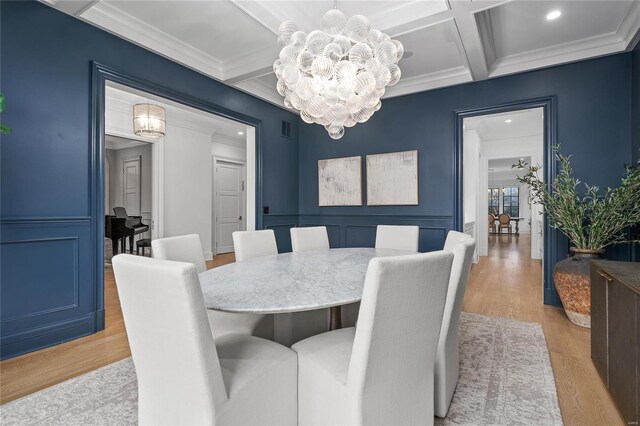 dining room with a chandelier, coffered ceiling, light wood-style flooring, and a decorative wall