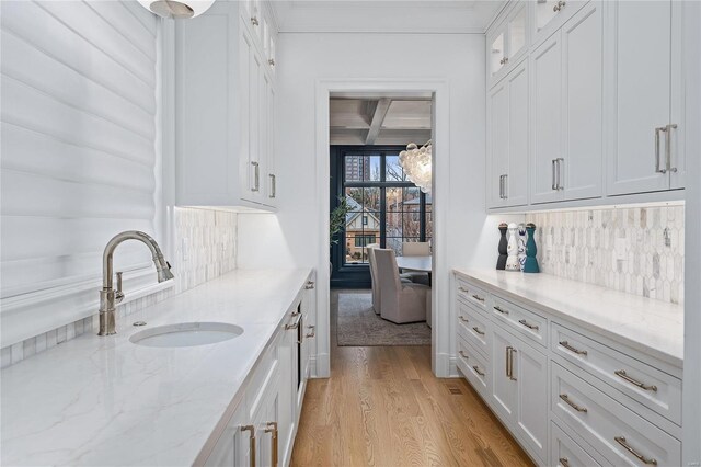 kitchen featuring coffered ceiling, glass insert cabinets, light wood-style floors, white cabinetry, and a sink