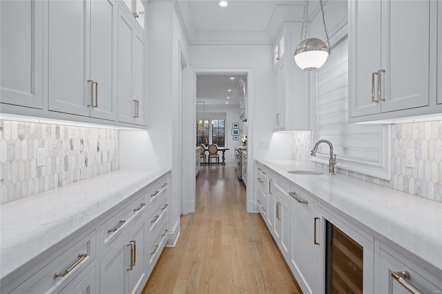 bar featuring light wood finished floors, backsplash, a sink, and decorative light fixtures