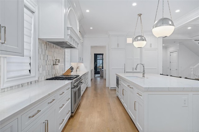 kitchen with an island with sink, white cabinets, range with two ovens, and hanging light fixtures