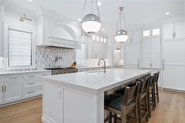 kitchen featuring light stone counters, an island with sink, glass insert cabinets, and white cabinetry