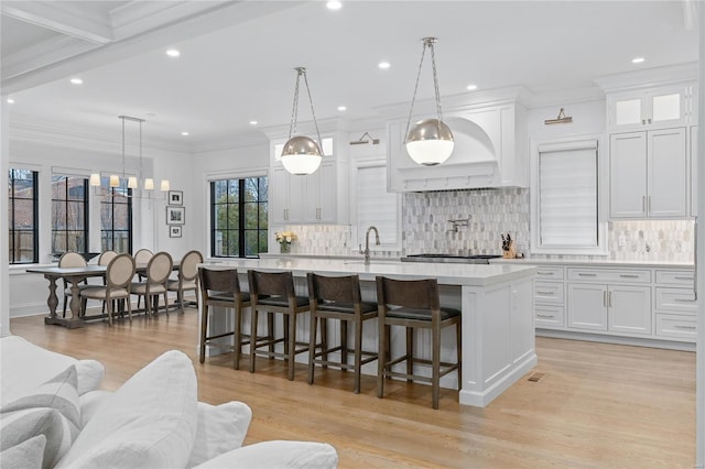 kitchen featuring a breakfast bar area, white cabinetry, light countertops, a center island with sink, and pendant lighting