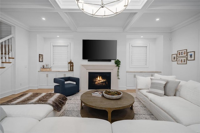 living room with a glass covered fireplace, coffered ceiling, a notable chandelier, and stairs