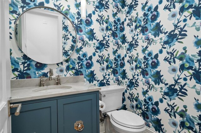 half bath featuring vanity, toilet, and wallpapered walls