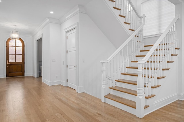 foyer entrance with arched walkways, crown molding, stairway, light wood-style flooring, and baseboards