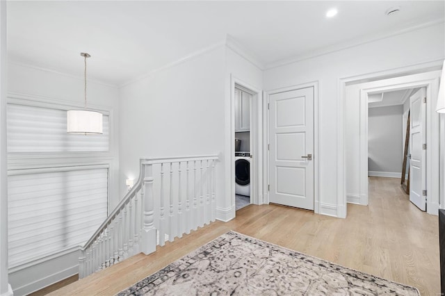 hall featuring washer / dryer, baseboards, wood finished floors, crown molding, and an upstairs landing