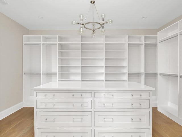 walk in closet with light wood-type flooring and an inviting chandelier