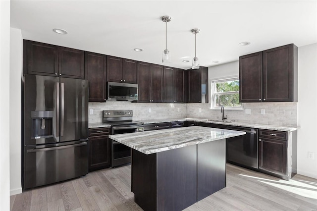 kitchen with sink, appliances with stainless steel finishes, light stone countertops, a kitchen island, and decorative light fixtures