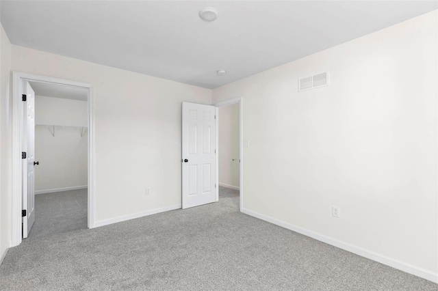 unfurnished bedroom with a walk in closet, light colored carpet, and a closet