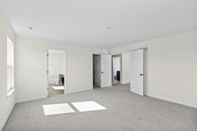 unfurnished bedroom with ensuite bathroom and light carpet